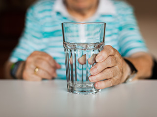 Wall Mural - Hand of senior lady holding a glass of water on table