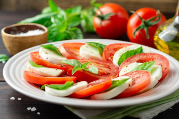 Wall Mural - Italian caprese salad with tomatoes, mozzarella cheese and basil in plate on dark wooden background