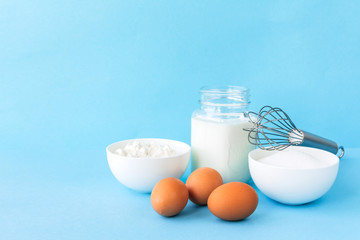 Eggs, flour, milk, sugar, and various ingredients for making pastry homemade pastry on a blue background with copy space