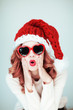 Leinwandbild Motiv Santas little helper. Beautiful happy young woman with a santa claus hat, perfect make up, red lipstick, and heart shape sun glasses, silly and funny mood 