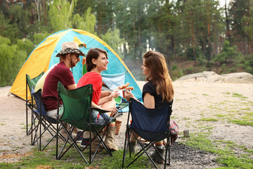 Young people having lunch with sausages near camping tent outdoors