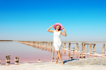 Wall Mural - Beautiful woman with hat posing near pink lake on summer day