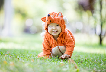 Wall Mural - Cute baby girl dressed in fox costume crawling on lawn in park