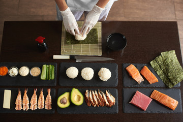 Close-up view of process of preparing rolling sushi. Nori and white rice. Chef's hands touch rice. Chef starts cooking sushi