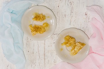 two white dessert plates with pieces of honeycomb on a light wooden background
