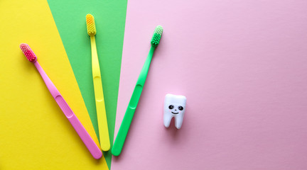 Plastic colorful toothbrushes and smiling tooth on a yellow, green, pink background. Dental care concept. Teeth care minimalism concept.