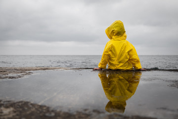 Wall Mural - Rainy clouds. Child in a yellow raincoat.