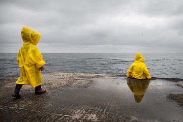  Rainy cloudy weather. Two children in yellow raincoats.