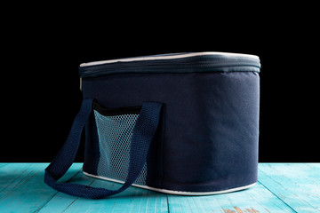 side view grey and blue lunch pack carrier on a wood table on black background