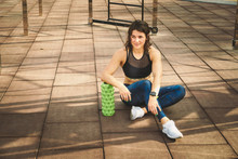 Theme Sport And Rehabilitation Sports Medicine. Beautiful Strong Slender Caucasian Woman Athlete Sits Next Foam Roller Green Field Street Workout To Remove The Pain, Stretch And Massage Muscles