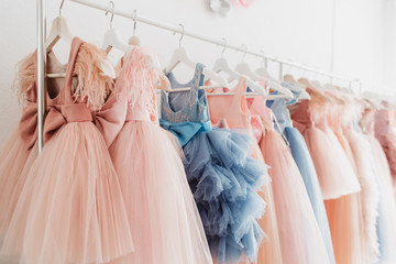 beautiful dressy lush pink and blue dresses for girls on hangers at the background of white wall. ki
