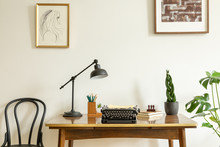 Framed Drawing On A White Wall Above An Antique, Wooden Desk With A Vintage, Black Typewriter In A Home Office Interior