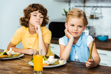 bored kids looking at asparagus while sitting at table with vegetables on plates