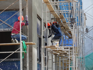 Wall Mural - Brick wall plastered by construction workers using the cement plaster. Scaffolding used as temporary staging to work at height. Wearing appropriate safety gear to prevent bad happen.  