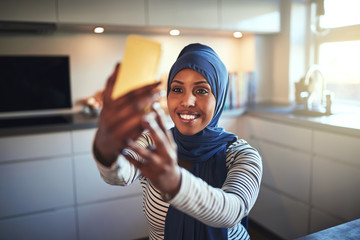 Wall Mural - Smiling young Arabic woman taking selfies in her kitchen