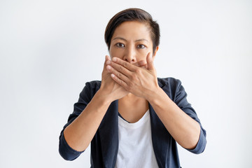 Sticker - Shocked Asian woman covering mouth with both hands. Young lady looking at camera. Shock concept. Isolated front view on white background.