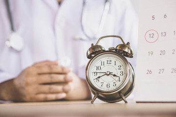 doctor appointment concept with alarm clock and calendar reminder note and doctor sitting in background 