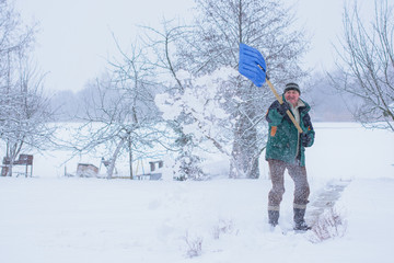 Winter, people and problem concept - closeup of man digging snow with shovel near car and yard. Man standing with blue shovel and he snow cleaning. Winter routine concept. 