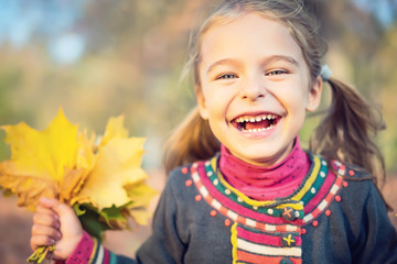 Portrait of happy little girl with autumn leaves in the park