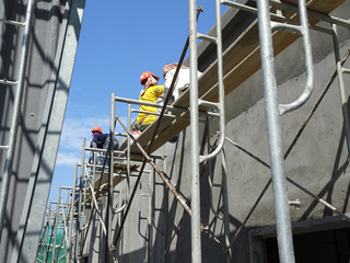 Wall Mural - Brick wall plastered by construction workers using the cement plaster. Scaffolding used as temporary staging to work at height. Wearing appropriate safety gear to prevent bad happen.  