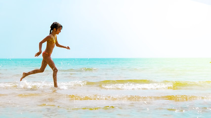 Summer fun beach woman splashing water. Panorama landscape of tropical ocean on travel holiday. Bikini girl running in freedom and joy with hands up enjoying the sun.