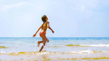 Summer fun beach woman splashing water. Panorama landscape of tropical ocean on travel holiday. Bikini girl running in freedom and joy with hands up enjoying the sun.