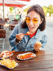 Wall Mural - Woman eating Currywurst fast food German sausage in outdoor street food cafe