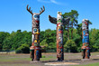 Three colorful wooden totem poles on green trees and blue sky background outdoors in park.