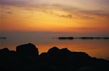 Wall Mural - rocky shore silhouette in the foreground. sunset view at the lake in the background.