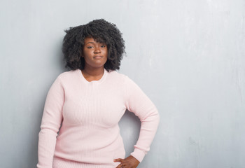 Sticker - Young african american plus size woman over grey grunge wall wearing winter sweater with serious expression on face. Simple and natural looking at the camera.