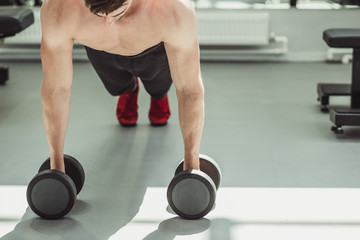 Caucasian fitness man with naked torso doing push-up exercise with dumbbell in fitness center