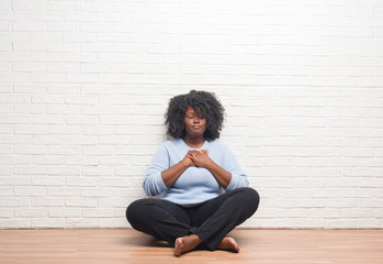 Canvas Print - Young african american woman sitting on the floor at home smiling with hands on chest with closed eyes and grateful gesture on face. Health concept.