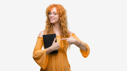 Sticker - Young redhead student woman holding a book very happy pointing with hand and finger