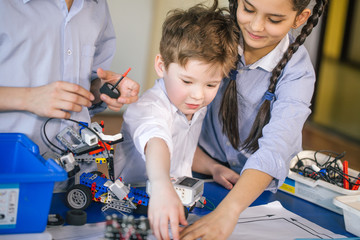 Wall Mural - Adorable blonde boy with his older friends visit kids show where they constructing a real small robots from metall details and electric chips. Technology, discovery, entertainment, children concept