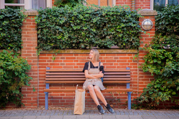 Young lady in dress sitting on bench with shopping bag on street of Bremen, Germany. Trevel destination concept