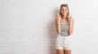 © Krakenimages.com - Young beautiful blonde woman over white brick wall smiling crossing fingers with hope and eyes closed. Luck and superstitious concept.