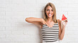 © Krakenimages.com - Beautiful young woman over white brick wall eating water melon slice with surprise face pointing finger to himself