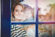 © Masson - Young girl with a child near a window at home in rainy day