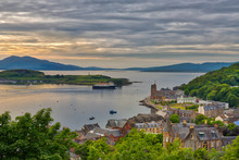 A Moody View From A Hill In The Port Town Of Oban, Scotland Looking Out On The Town And The Water With The Isle Of Mull In The Distance With A Hint Of The Summer Sunset And Grey Clouds