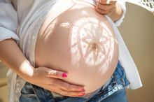 Pregnancy. A Pregnant Woman Holds An Openwork White Umbrella And Covers Her Belly From The Sun. On The Stomach Lies A Shadow In The Form Of A Patterned Flower.