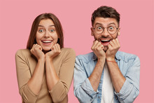 Shot Of Glad Young Brother And Sister Keep Hands Under Chin, Have Broad Smiles, Rejoice Good News, Dressed In Casual Clothes, Isolated Over Pink Background, Express Happiness. Wow, Thats Great!