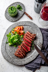 Wall Mural - Grilled beef steak medium rare slices on gray stone plate with salad and chimichurri sauce