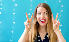Young Woman Giving The Peace Sign On A Shiny Light Background