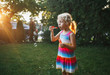 © anoushkatoronto - Candid portrait of cute funny little blond Caucasian child girl blowing soap bubbles on home backyard at summer sunset. Real authentic happy childhood moment. Toned with film filters.