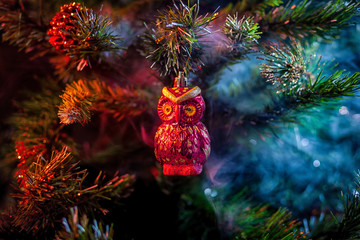 Sticker - Red shiny decoration Christmas balls owl with house in colored purple-red smoke, on an  christmas tree background. Concept of a modern Christmas card.