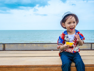 Cute happy asian boy in a summer shirt eating yellow lemon in hand on the wooden table posing background of Hua Hin sea blue skyThailand.Copy-space for your edit.