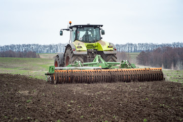 A tractor pulls a disc harrow system implement to smooth over a dirt field in preparation for planting