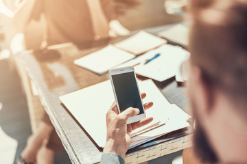 Poster - Close up male hand holding contemporary cellphone in hand. He looking at screen of appliance. Different documents locating on table
