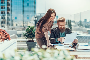 Poster - Portrait of positive woman and cheerful bearded male talking, while looking at document outside. Employer pointing on it during communication