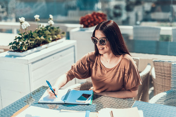 Poster - Portrait of beaming girl writing in copybook while sitting at table in cozy cafe during labor outdoor